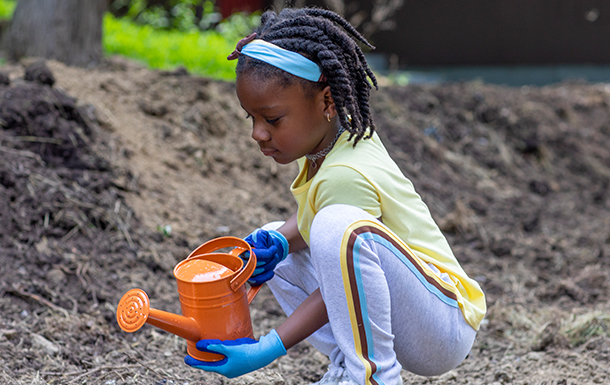 young girl scout gardening with orange watering can outdoors at park